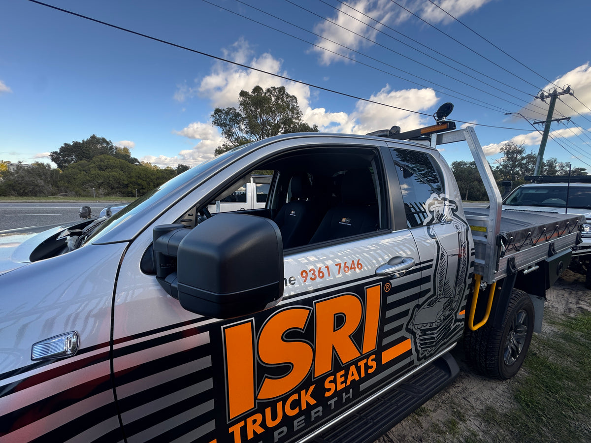 Service truck cab and open bed with orange decals, parked under power lines in a blue sky